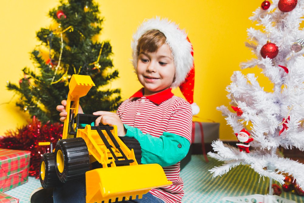 A young boy wearing a Santa hat engages with a toy bulldozer, amidst thrilling dinosaur excavator and transformer RC cars.