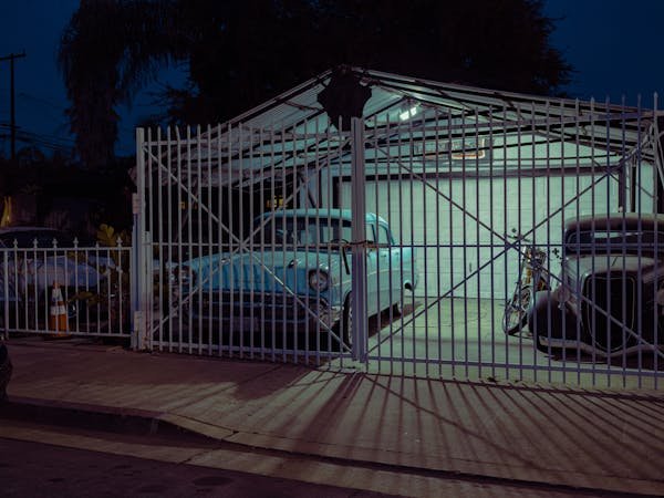 A white fence with a gate encloses a driveway where a car is parked, showcasing a completed fence and garage gate installation.